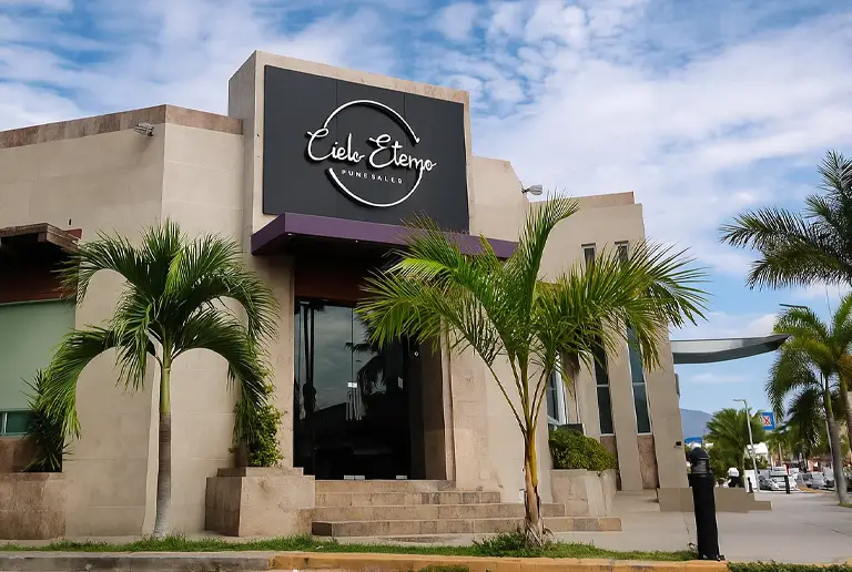 Exterior del edificio de Cielo Eterno Manzanillo con palmeras y cielo despejado.