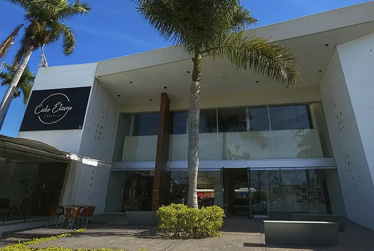 Fachada de la sede de Cielo Eterno Colima con palmeras y cielo azul.