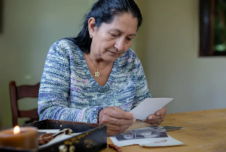 Mujer mexicana mirando una fotografía con expresión de tristeza y esperanza, rodeada de recuerdos en una mesa. Imagen sobre duelo por desaparición forzada.