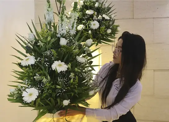 Asesora funeraria preparando arreglo floral blanco para homenaje póstumo, como parte de una ceremonia para honrar la vida