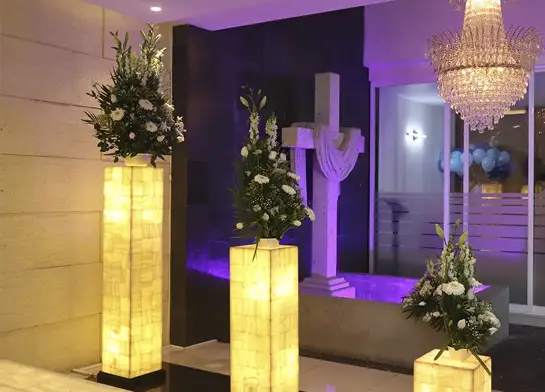 Sala de homenaje con arreglos florales y cruz iluminada, espacio para ceremonias funerarias que celebran la vida con respeto y elegancia