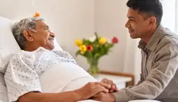 Acompañamiento emocional antes del fallecimiento: un hijo toma la mano de su padre en etapa terminal, compartiendo un momento íntimo y lleno de amor.