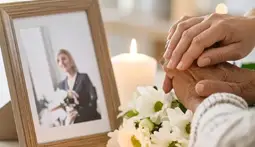 Contención emocional en el momento del fallecimiento: manos unidas junto a una fotografía con velas y flores, símbolo de apoyo y presencia en el adiós.